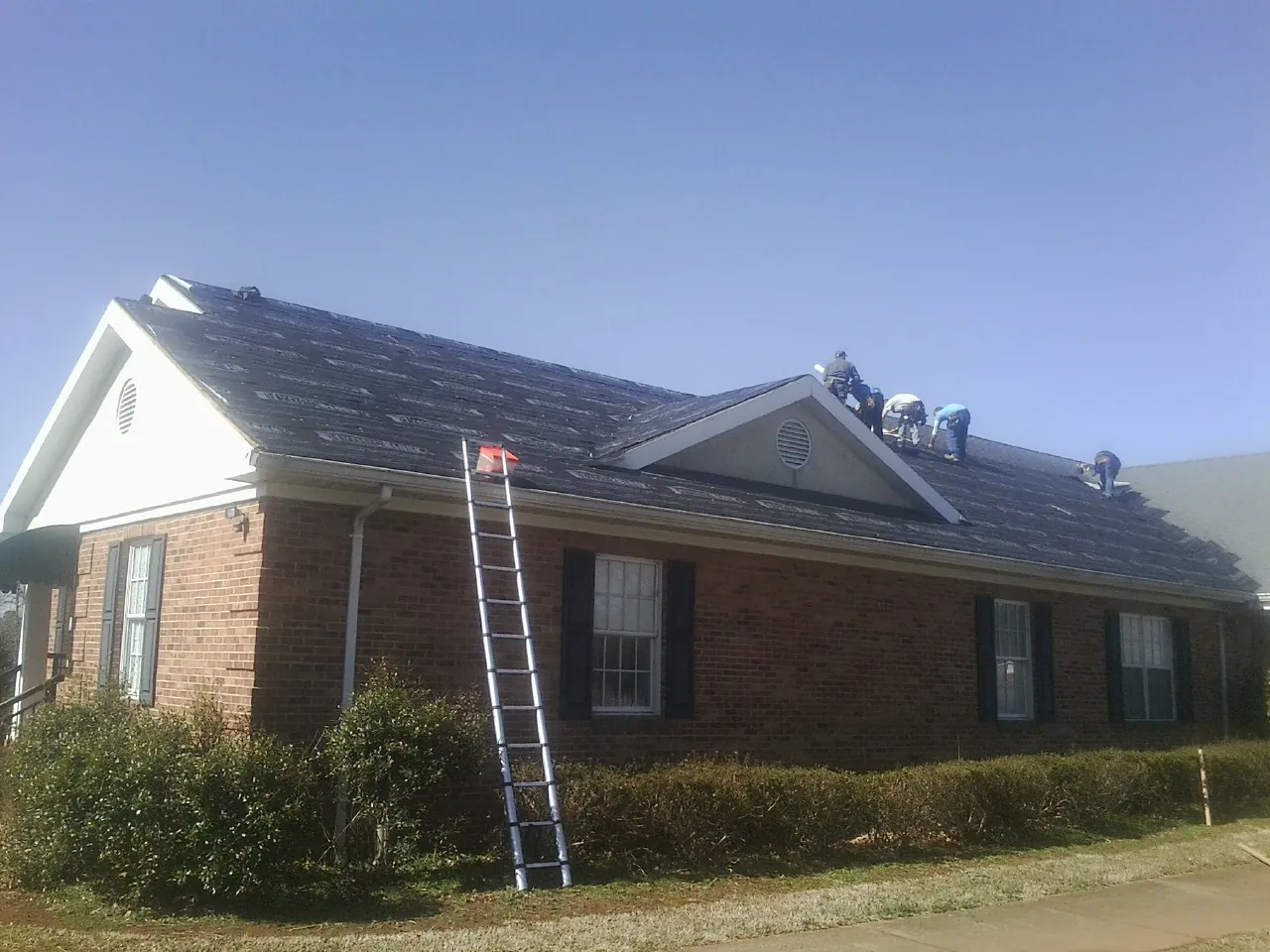 Crew tearing shingles off a brick ranch roof with a ladder set — Metal Roof Repair work by our crew in Tennessee Ridge