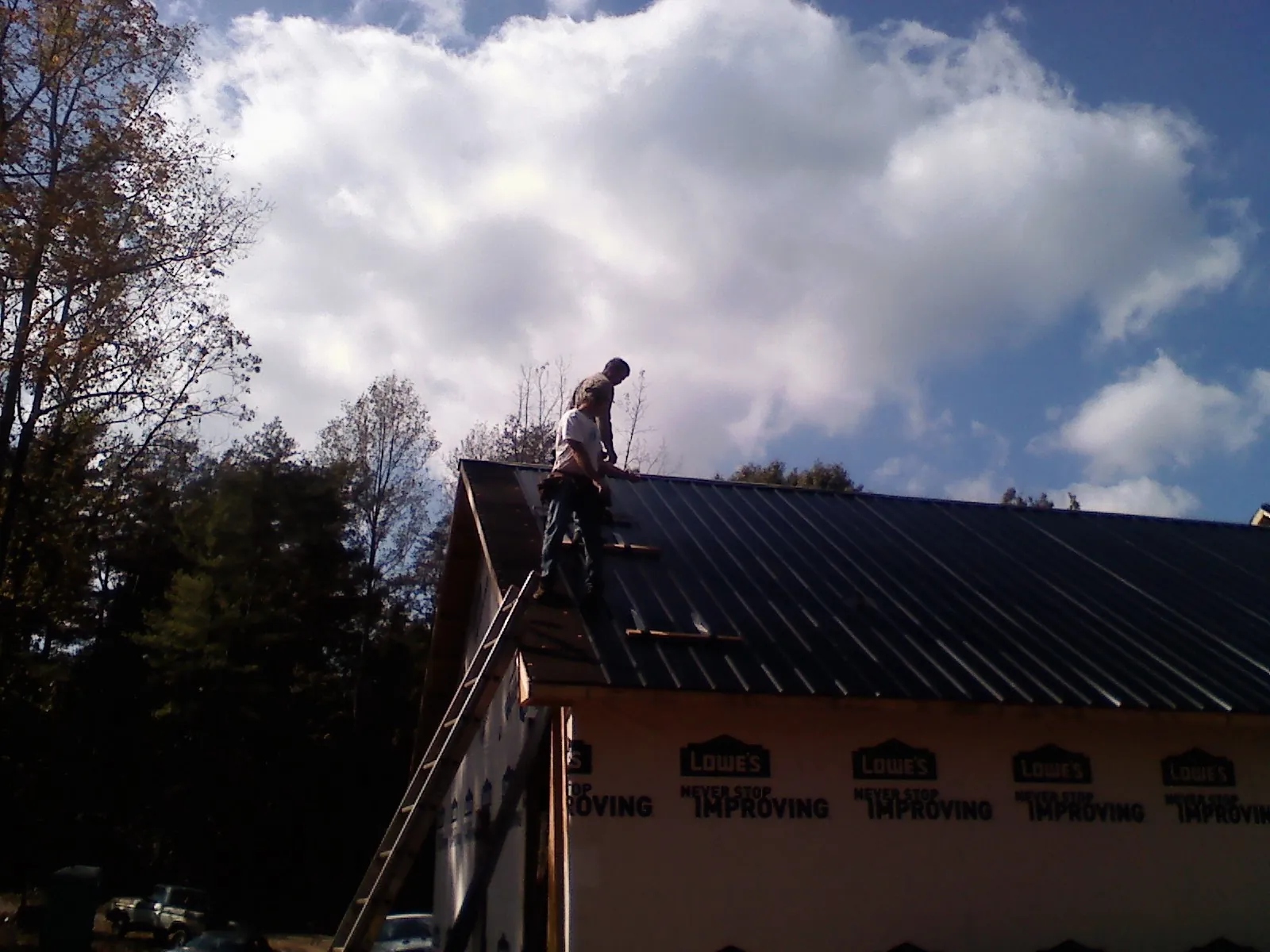 Roofer fastening dark metal panels high against a cloudy sky, from a Roof Inspection job in Tennessee Ridge