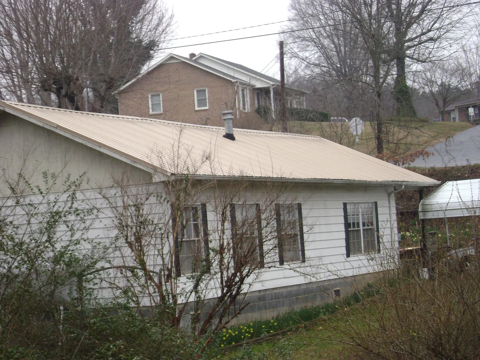 Tan metal roof on a white sided house set into a hillside — Commercial Roofing by Roofing Brothers in Tennessee Ridge